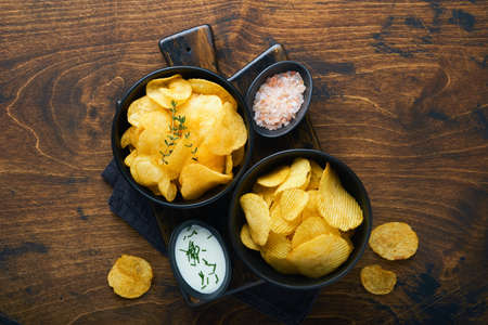 Potato chips. fast food. Crispy potato chips ceramic black bowl with sour cream sauce and onions in wooden stand on old kitchen table wooden background. American tradition. Hot BBQ. top view.の写真素材