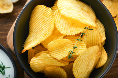 Potato corrugated chips. fast food. Crispy potato chips ceramic black bowl with sour cream sauce and...