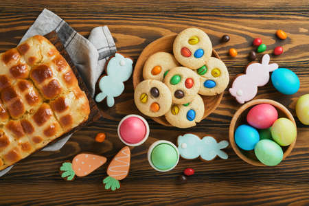 Easter hot cross buns with colored eggs Easter gingerbread rabbits and cookies over dark brown plank wooden old table background. Spring holiday baking concept. Easter table setting. top view. Mock upの写真素材