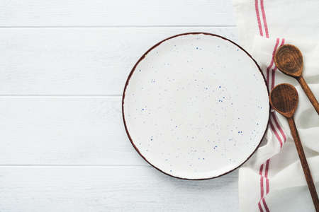 Ceramic empty white plate. Rustic vintage set of white plate, wooden spoon on light white wooden...