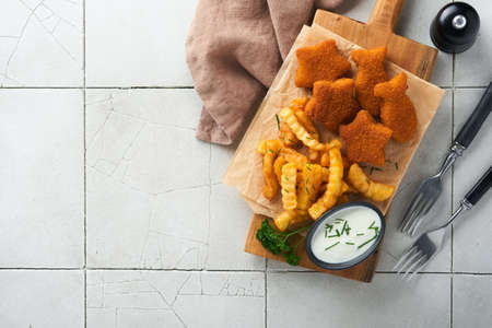 Fish Chips british fast food. Fish Sticks with french fries set server on rustic board on old gray cracked tile countertop table background. Traditional British authentic street food, takeaway food.の写真素材