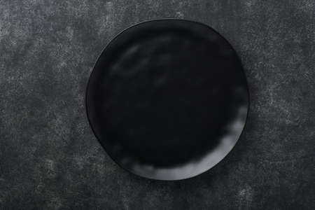 Ceramic empty black plate on old black ceramic cement concrete table background. Cooking stone backdrop. Top view with copy space. flat layの写真素材