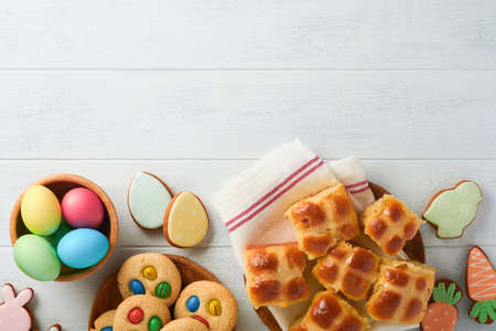Easter hot cross buns with colored eggs, Easter gingerbread rabbits and cookies over white plank...