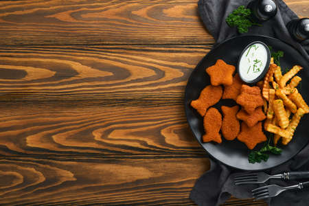 Fish and Chips british fast food. Fish Sticks with french fries set on black plate on old wooden table background. Traditional British authentic street food or takeaway food. Mock up. Space for text.の写真素材