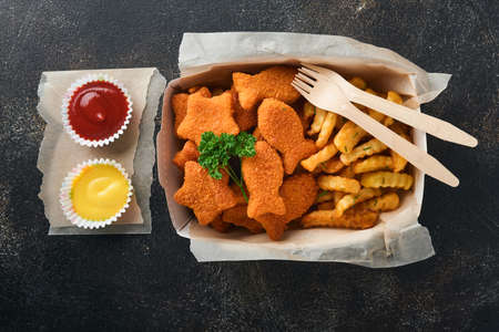 Fish and Chips british fast food. Fish Sticks with french fries set on takeaway paper plate on dark old concrete background. Traditional British authentic street food or takeaway food. Mock up.の写真素材