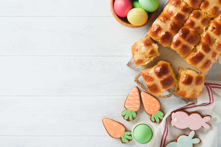Easter hot cross buns with colored eggs, Easter gingerbread rabbits and cookies over white plank...