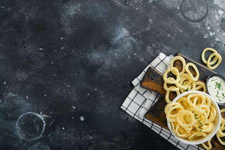 Onion rings. fast food. Crispy onion chips in ceramic black bowl with sour cream sauce and onions in wooden stand on old black concrete background. American tradition. Hot BBQ. top viewの写真素材