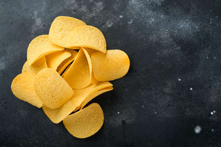 Potato corrugated chips. fast food. Crispy potato chips ceramic black bowl with sour cream sauce and onions in wooden stand on old black concrete background. American tradition. Hot BBQ.の写真素材