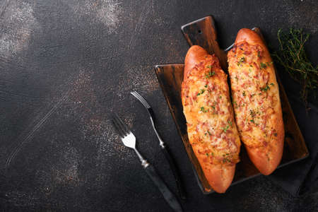 Baguette boats. Hot baked sandwich on baguette bread with ham, bacon, vegetables and cheese on parchment and black dark concrete background. top view. copyspace.の写真素材