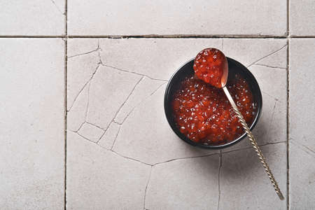 Red salmon caviar. Delicious red caviar in black bowl on old cracked tile table background. Top view...