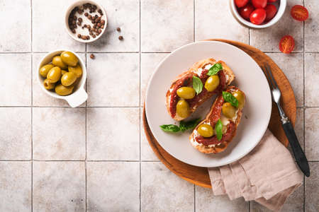 Bruschetta with dried sun tomatoes. Toast or sandwich with ricotta, sun dried tomatoes and Provence herbs with basil servered on a plate on a gray old cracked tile table. Top view banner menu recipe.の写真素材