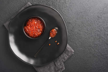 Red salmon caviar. Delicious red caviar in black bowl on black dark concrete background. Top view...