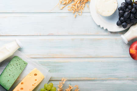 Shavuot jewish holiday celebration. Milk and cheese, ripe wheat and fruits, blue wooden background. Dairy products over blue wooden background. Shavuot concept. top view. Mock up.の写真素材