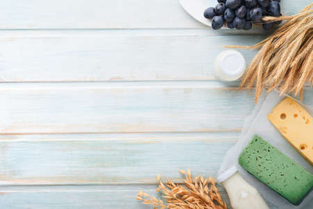 Shavuot jewish holiday celebration. Milk and cheese, ripe wheat and fruits, blue wooden background. Dairy products over blue wooden background. Shavuot concept. top view. Mock up.の写真素材
