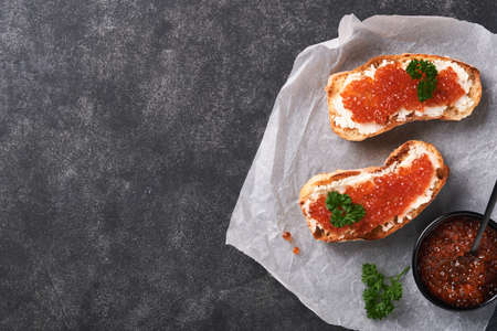 Two sandwiches with red caviar. Salmon red caviar in bowl and sandwiches server on old parchment paper on old black table background. top view. copyspace.の写真素材