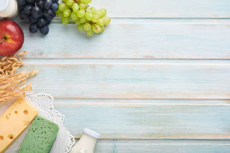 Shavuot jewish holiday celebration. Milk and cheese, ripe wheat and fruits, blue wooden background....