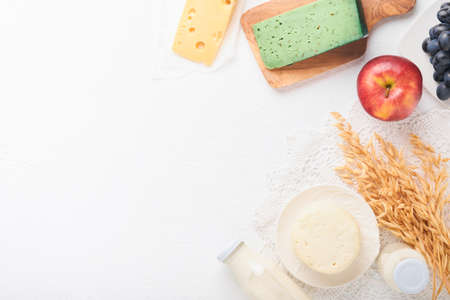 Shavuot jewish holiday celebration. Milk and cheese, ripe wheat and fruits, blue wooden background. Dairy products over white concrete background. Shavuot concept. top view. Mock up.の写真素材