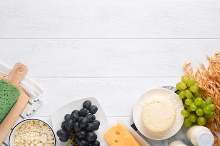 Shavuot jewish holiday celebration. Milk and cheese, ripe wheat and fruits, cream. Dairy products over white wooden background. Shavuot concept. top view. Mock up.の写真素材