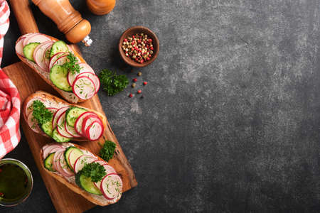 Toast with cheese and radish. Sandwiches with cottage cheese, radish, cucumber and green onions on old dark stone table background. Healthy spring sandwiches. Traditional Scandinavian toast. top viewの写真素材