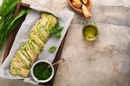 Braided wild garlic pesto brioche. Homemade raw or uncooked fresh pull apart bread with wild garlic pesto on wooden board on old gray background table. Italian bread. copyspace. top view.の写真素材
