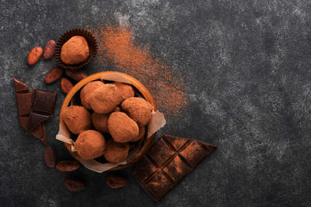 Chocolate truffles with cocoa powder in wooden dish on old dark concrete table background. Tasty sweet chocolate truffles candies. Valentines Day and Mothers Day concept with copy space. top view.の写真素材