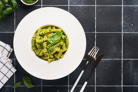 Italian Fusilli Pasta with Pesto. Fusilli pasta with basil pesto and herbs, parmesan cheese, basil and garlic on white plate on black stone countertop background. top view. copyspace. Mock up.の写真素材