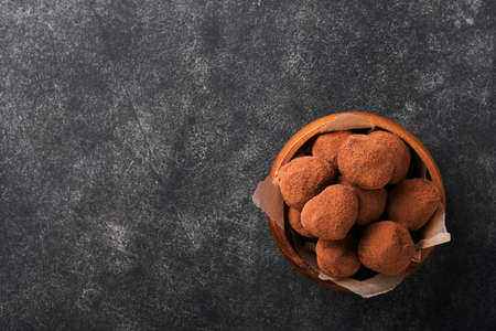 Chocolate truffles with cocoa powder in wooden dish on old dark concrete table background. Tasty sweet chocolate truffles candies. Valentines Day and Mothers Day concept with copy space. top view.の写真素材