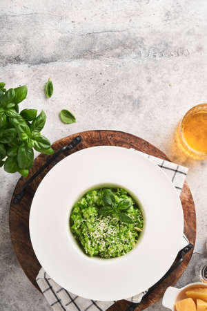 Italian risotto. Delicious risotto in white plate with pesto sauce or wild garlic pesto, basil, parmesan cheese and glass of white wine on old light gray table background. Top view with copy space.の写真素材