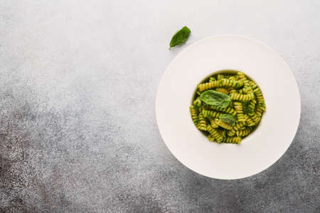 Italian Fusilli Pasta with Pesto. Fusilli pasta with basil pesto and herbs, parmesan cheese, basil and garlic on white plate on gray stone countertop background. top view. copyspace. Mock up.の写真素材