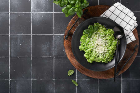 Italian risotto. Delicious risotto with pesto sauce or wild garlic pesto, basil, parmesan cheese and glass of white wine on old black tiles table background. Italian dinner. Top view with copy space.の写真素材