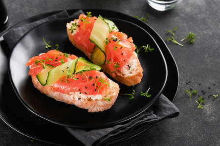 Sandwiches. Salmon toast with cream cheese, cucumber, black sesame and microgreens on black background. seafood. Health food. Photography in low key. top view.の写真素材