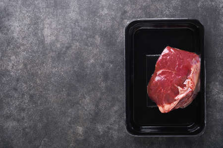 beef steak. Fresh raw beef steak in vacuum black plastic pack on black stone background. Vacom package. top view. Mockup for design idea.の写真素材