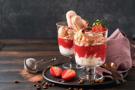 Strawberry tiramisu. Traditional Italian dessert tiramisu in glass with fresh strawberry and mint leaves on old wooden dark table background. copyspace. food background.の写真素材