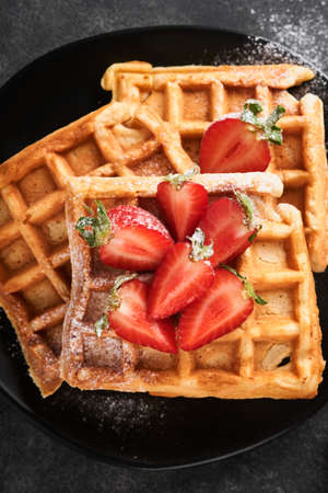 Belgian waffles. Homemade waffles with strawberries, powdered sugar and cup of coffee on black plate...