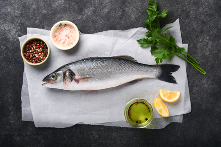 Sea bass raw. Fresh sea fish bass with salt, pepper, parsley, olive oil and lemon on parchment paper...