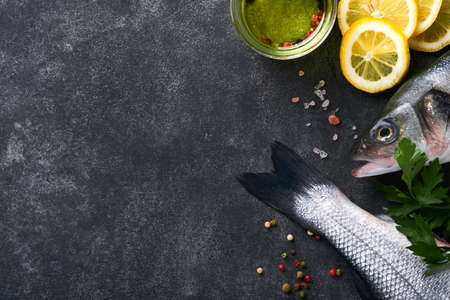 Sea bass raw. Fresh sea fish bass with salt, pepper, parsley, olive oil and lemon on dark concrete rustic background. Fresh fish ready to cook. food cooking background. Top view, copy space.の写真素材