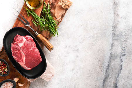 beef steak. Fresh raw beef rib eye steak with fork rosemary, salt and pepper on a grill pan on gray stone background. top view. Mockup for design idea.の写真素材