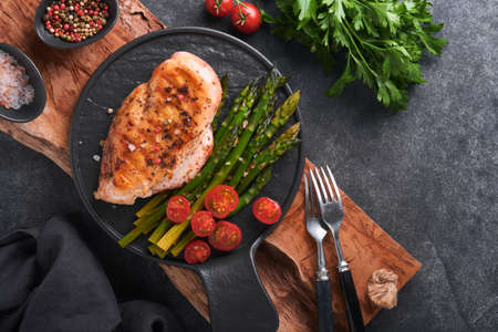 Chicken breast grilled with vegetables. Grilled chicken steak, asparagus and cherry tomatoes in black plate on gray concrete table background. Healthy diet lunch. Barbecue steak fried. top view.の写真素材