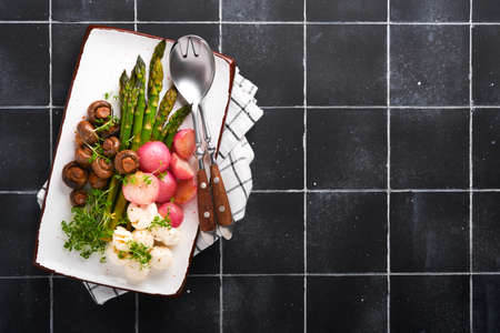 Asparagus, mushrooms, mozzarella cheese, grilled radish and cress salad, oil olive salad on rectangular ceramic plate on black old tile table background. Healthy diet grilled food concept. top view.の写真素材