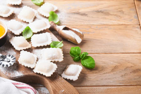 Ravioli Italian food. Tasty homemade pasta ravioli with flour, tomatoes, eggs and greens basil on wooden background. Process of making italian ravioli. Food cooking ingredients background. top view.の写真素材