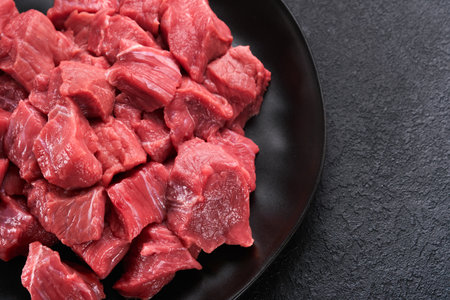 Raw chopped beef meat. Raw organic meat beef or lamb, spices, herbs on black plate on dark gray concrete background. Goulash. Raw uncooked meat. Meat with blood. Top viewの写真素材