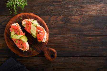 Sandwiches. Salmon toast with cream cheese, cucumber, black sesame and microgreens on old wooden table background. seafood. Health food. Photography in low key. top view.の写真素材