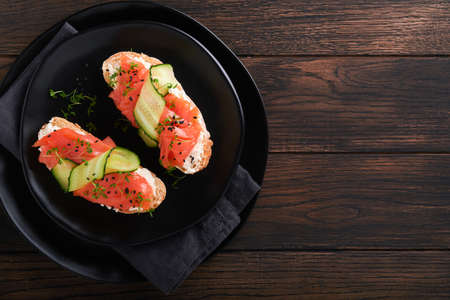 Sandwiches. Salmon toast with cream cheese, cucumber, black sesame and microgreens on old wooden table background. seafood. Health food. Photography in low key. top view.の写真素材