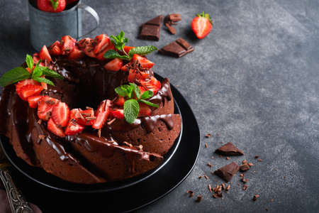 Dark Chocolate Bundt Cake with Ganache Icing and strawberry on dark stone or concrete table background. Festive cake. selective focusの写真素材
