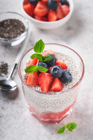 Chia strawberry pudding. Healthy vegan breakfast chia seeds pudding with fresh berries and mint in glass on gray concrete background. Concept of healthy eating, dieting, fitness menu. selective focus.の写真素材