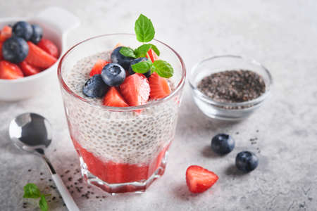 Chia strawberry pudding. Healthy vegan breakfast chia seeds pudding with fresh berries and mint in glass on gray concrete background. Concept of healthy eating, dieting, fitness menu. selective focus.の写真素材