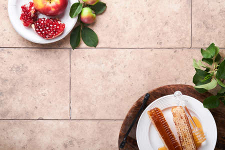 Rosh Hashanah. Honey jar, honeycomb, apple and pomegranate on light beige old rustic concrete...