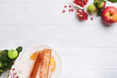 Rosh Hashanah. Honey jar, honeycomb, apple and pomegranate on white wooden old rustic background table. Jewish New Year holiday greeting card. Rosh Hashanah holiday attributes. Space for textの写真素材