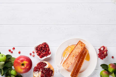 Rosh Hashanah. Honey jar, honeycomb, apple and pomegranate on white wooden old rustic background...