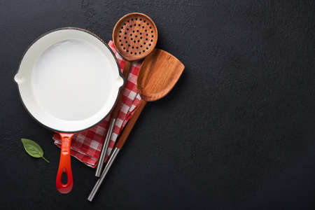 Frying pan white , black empty plate, basil leaves and spices on dark stone background. Abstract food background. Top view of dark rustic kitchen table with wooden cooking utensils, frame. Mock up.の写真素材